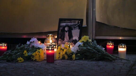 Brennende Grabkerzen, Blumen und ein Bild eines verstorbenen Mannes stehen am Geländer einer Brücke in Halle an der Saale.