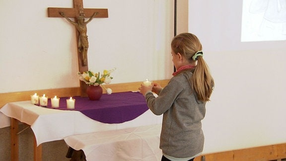 Ein Kind stellt eine Kerze an ein Kreuz.