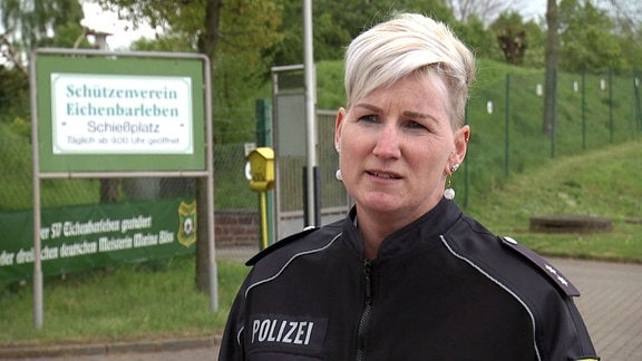 Polizistin im Interview, im Hintergrund das Gelände eines Schützenvereins.