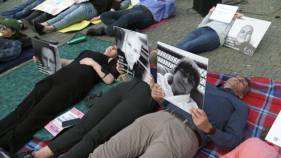 Demonstranten liegen und halten Portraitfotos in den Händen.