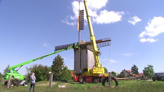 Ein Kran hebt einen Flügel an die Windmühle heran.