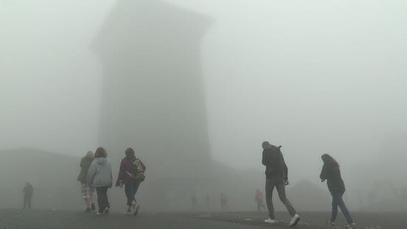 Menschen erreichen bei Nebel die Spitze des Brockens.