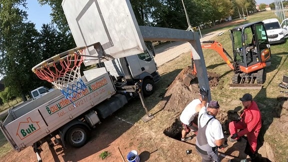 Arbeiter stellen einen Basketballkorb auf.