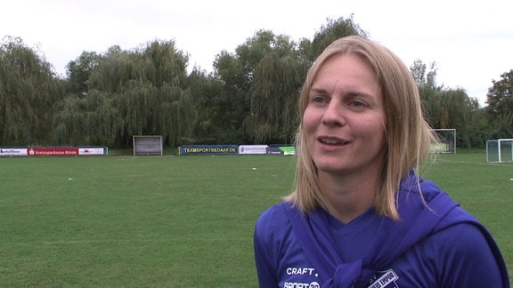 Eine junge Frau während Interview, im Hintergrund ein Fußballfeld.