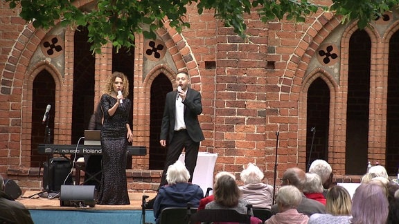 Eine Frau und ein Mann singen vor Publikum.