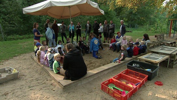 Kinder und Erwachsene sitzen in einem großen Sandkasten.