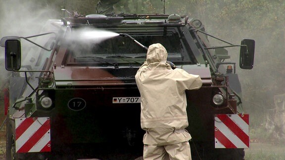 Soldat in Schutzkleidung beim Dekontaminieren eines Fahrzeugs