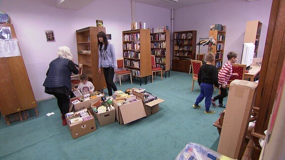 Erwachsene und Kinder räumen in einer Bibliothek.