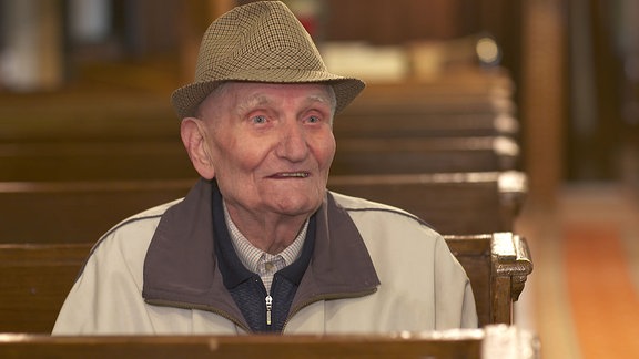 Ein Mann mit Hut sitzt in einer Kirche.