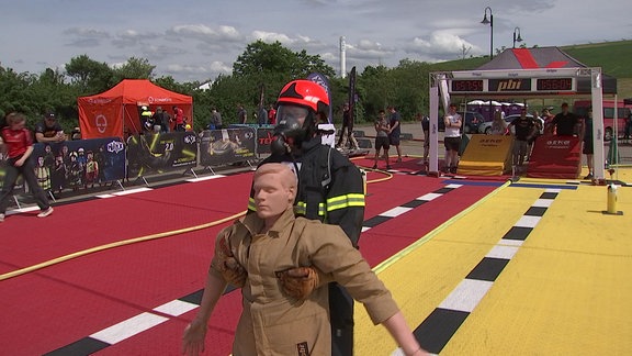 Bei einem Wettkampf zieht eine Person in Feuerwehruniform eine Puppe.