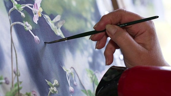 Ein Blumenmotiv wird auf eine Leinwand gemalt