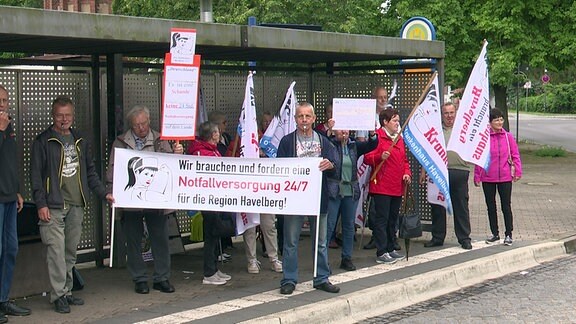 Mitglieder des Vereins Pro Krankenhaus Havelberg stehen mit Transparenten an einer Haltestelle