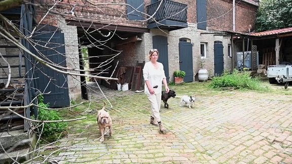 Eine Frau läuft mit drei Hunden über einen Hof.