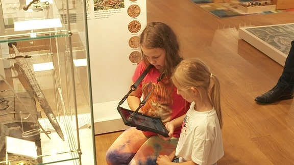 Zwei Mädchen sitzen in Museum und nutzen ein Tablet