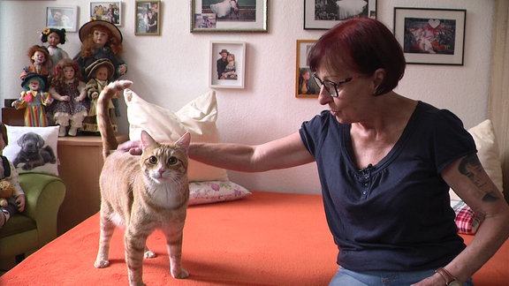 Frau sitzt auf Bett und streichelt eine Katze