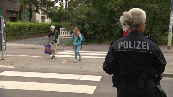 Eine Polizistin steht an einem Zebrastreifen, an dem Schulkinder die Straße überqueren.