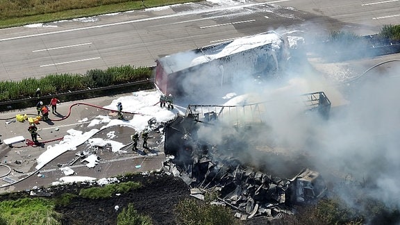 Einsatzkräfte der Feuerwehr löschen an einer Unfallstelle auf der Autobahn.