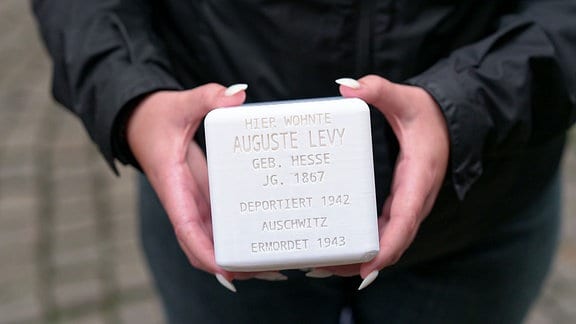 Eine Frau hält einen weißen Stolperstein