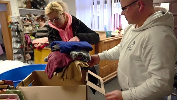 Eine Frau und ein Mann packen Kleidung in eine Kiste