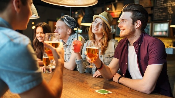 Junge Leute sitzen am Tresen und feiern mit alkoholischen Getränken.
