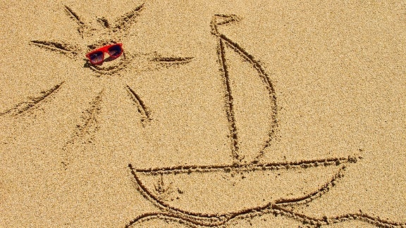 Eine Sonne und ein Segelboot sind in den Sand an einem Strand gemalt