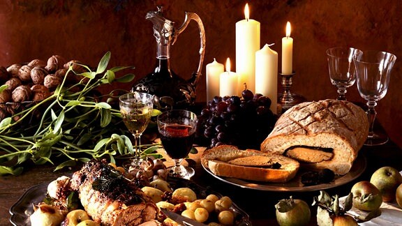 Ein weihnachtliches Festmal (Braten, Brot, Wein, ...) ist auf einem Tisch arrangiert.
