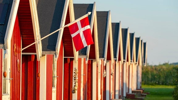 Die dänische Flagge und rote Fischerhütten an der Ostseeküste.