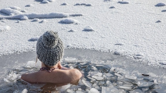 Eine Frau beim Eisbaden bei einer gefrorenen Wasserfläche im Winter. 
