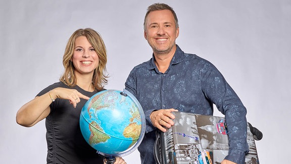 Porträt von Elena Pelzer und Silvio Zschage die einen Globus und einen Koffer halten.