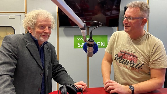 Sprecher Christian Steyer und MDR-Reporter Dirk Hentze an einem Pult in einem Studio