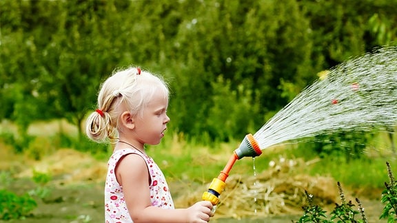 Ein Mädchen gießt im Garten mit einer Brause.