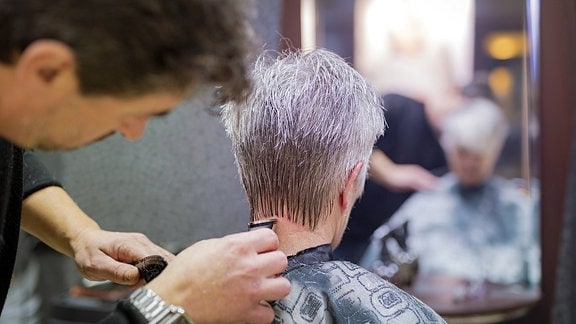 Ein Friseur schneidet die Haare einer grauhaarigen Frau.