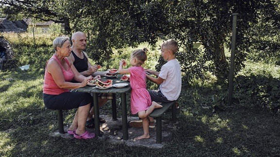 Großeltern sitzen mit ihren Enkeln an einem Gartentisch.