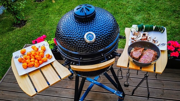 Ein Kamado-Ei-Grill auf der Terrasse eines Wohnhauses, auf dem Rindersteaks und Gemüse zubereitet werden sollen.