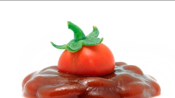 Eine Tomate steckt in einer Ketchuplache.