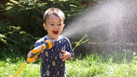 Ein Kind hält lachend einen Gartenschlauch.