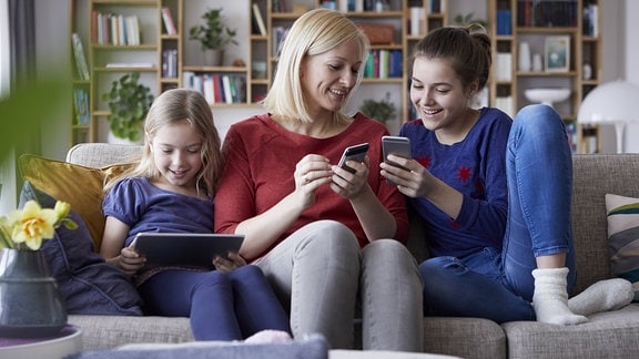 Mutter sitzt mit ihren zwei Töchtern auf der Couch.