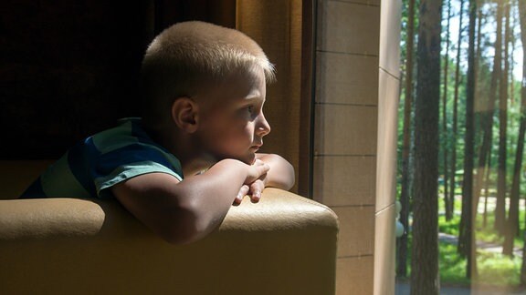 Junge schaut traurig aus dem Fenster.