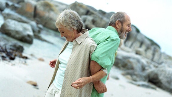 Älteres Ehepaar hat sich Rücken an Rücken untergehakelt und lacht