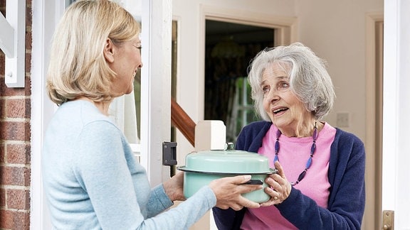 Eine Frau überreicht einer anderen einen Topf an der Haustür.
