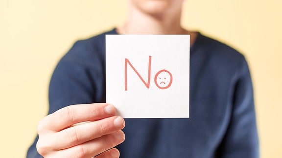 Ein Zettel mit der Aufschrift 'No' wird von einer Hand gehalten.