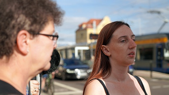 Auf dem Bild sind Rehabilitationslehrerin Ulrike Schade und Schülerin Nancy zu sehen (v.l.n.r.), wie sie an einer Straße stehen. Nancy versucht herauszufinden, von wo nach wo sich die Fahrzeuge vor ihr bewegen.