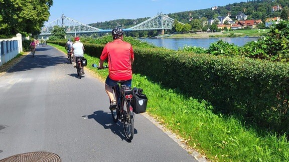 Menschen fahren auf Fahrrädern den Elberadweg entlang. Im Blick: das Blaue Wunder.