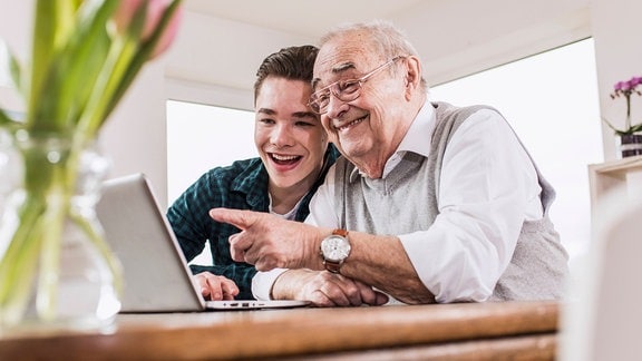 Glücklicher älterer Mann und Enkel im Gespräch am Laptop