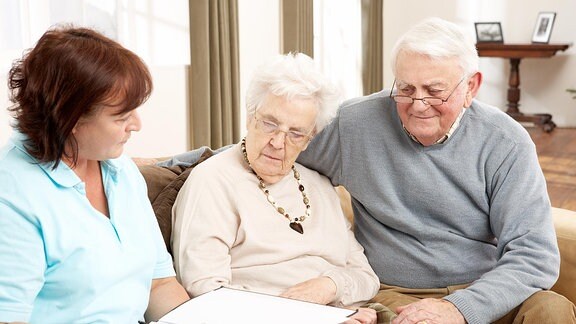 Ein Seniorenpaar sitzt mit einer Pflegerin zusammen.