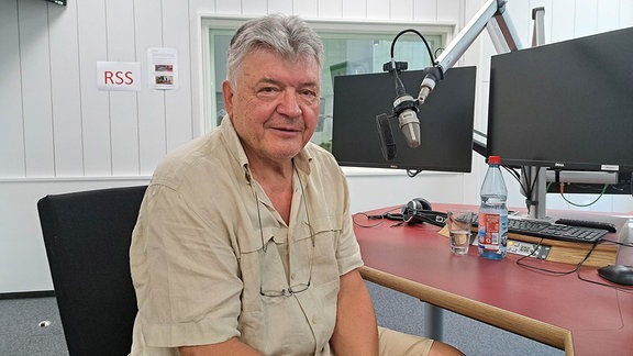 Ein Mann mit kurzen grauen Haaren sitzt in einem Radiostudio.