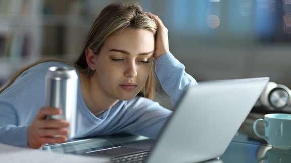 Eine Frau sitzt an ihrem Laptop mit einer Dose in der Hand.