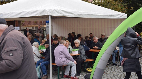 Menschen sitzen unnter einem Pavillon.