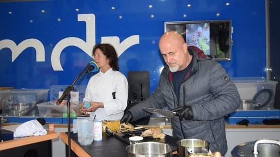 Ein Mann und eine Frau an einem Tisch vor blauem Hintergrund