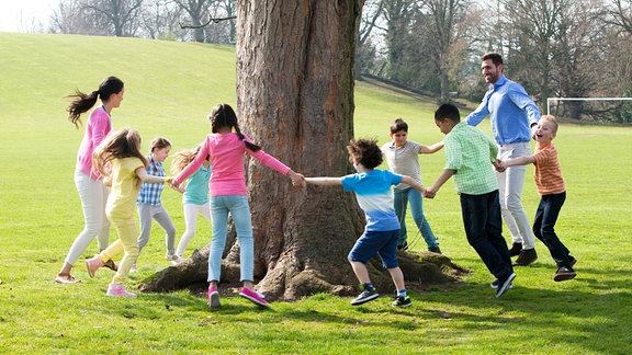 Kinder tanzen um einen Baum